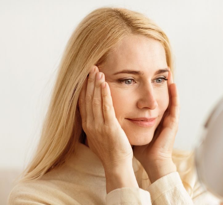 Woman examining crow's feet around her eyes in a mirror